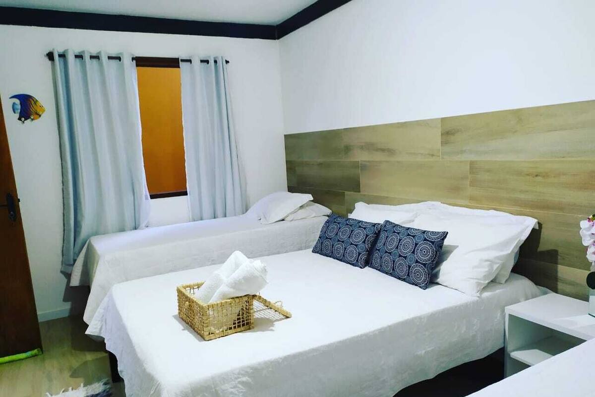 A hotel room with two beds, a wooden headboard, a window with curtains, and a small table with a basket and a towel.