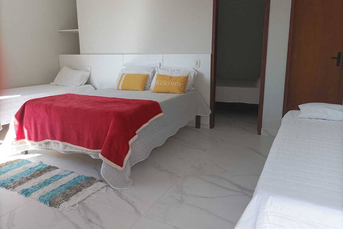 A hotel room with two beds, a red blanket on one bed, a striped rug, and a door leading to another room.