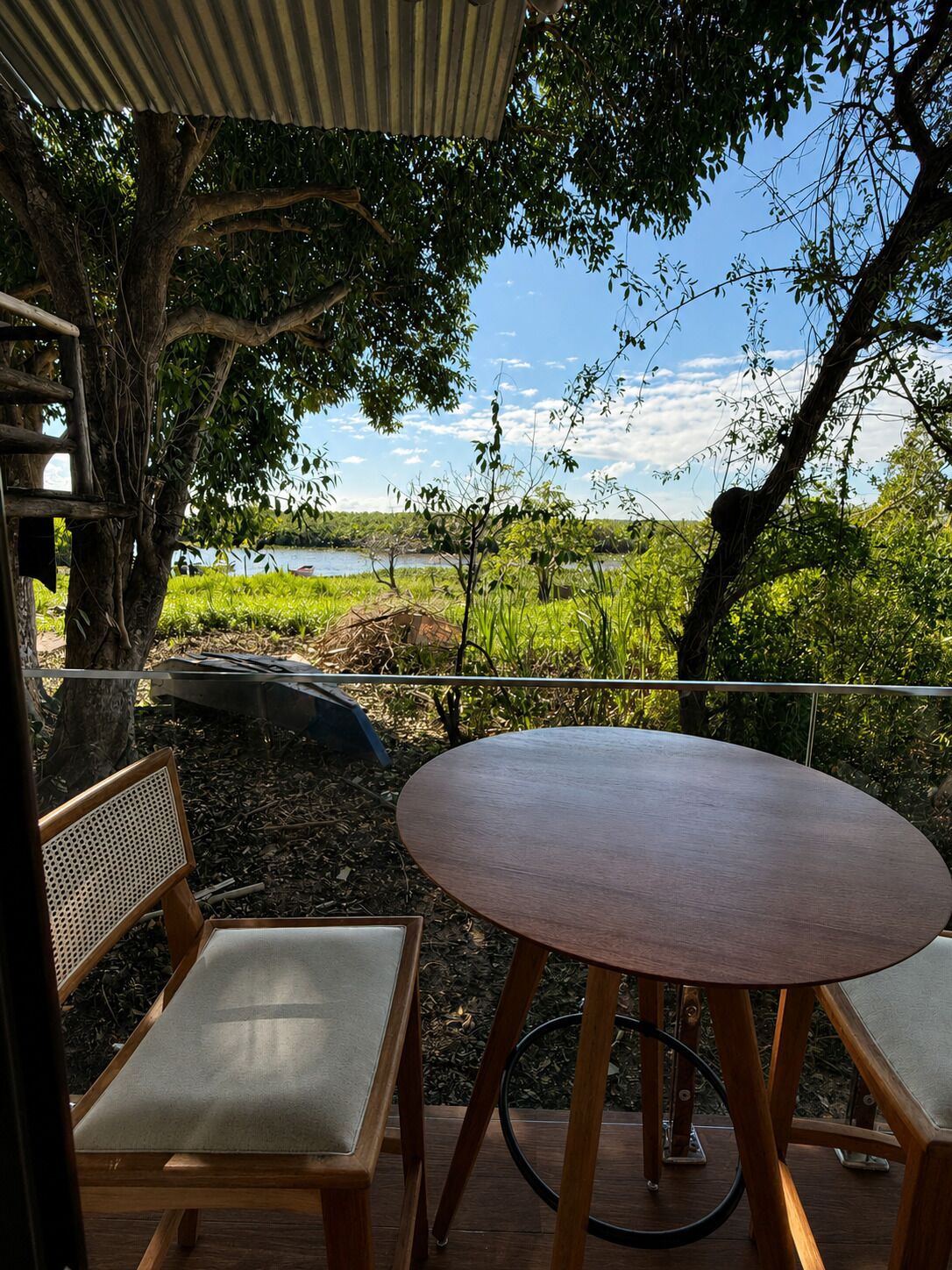 Un espacio al aire libre con mesa y sillas, rodeado de árboles y vista hacia un cuerpo de agua.