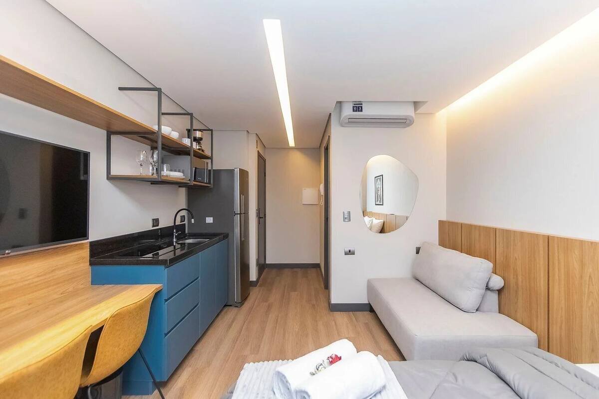 Une petite cuisine équipée comprenant un réfrigérateur, un évier et un four à micro-ondes, un lit avec une tête de lit et une petite table de chevet.