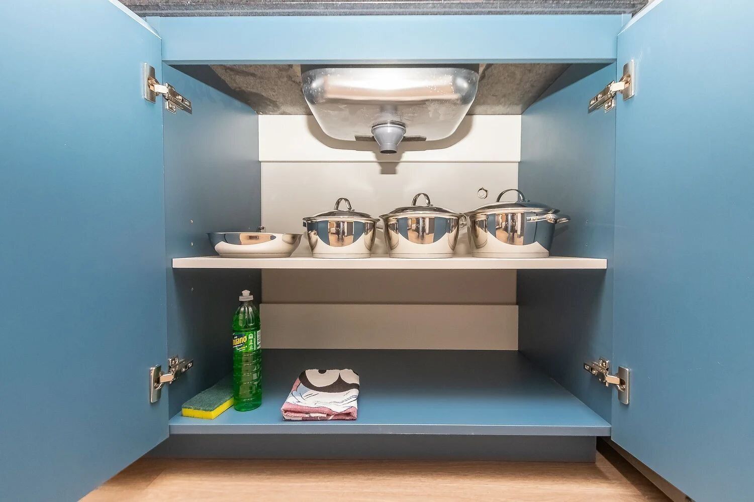 Una cocina con un armario azul, un lavabo y ollas de acero inoxidable sobre la encimera.