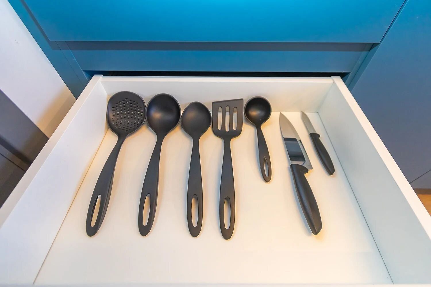 A drawer containing black kitchen utensils including a spatula, spoon, ladle, fork, and knife.