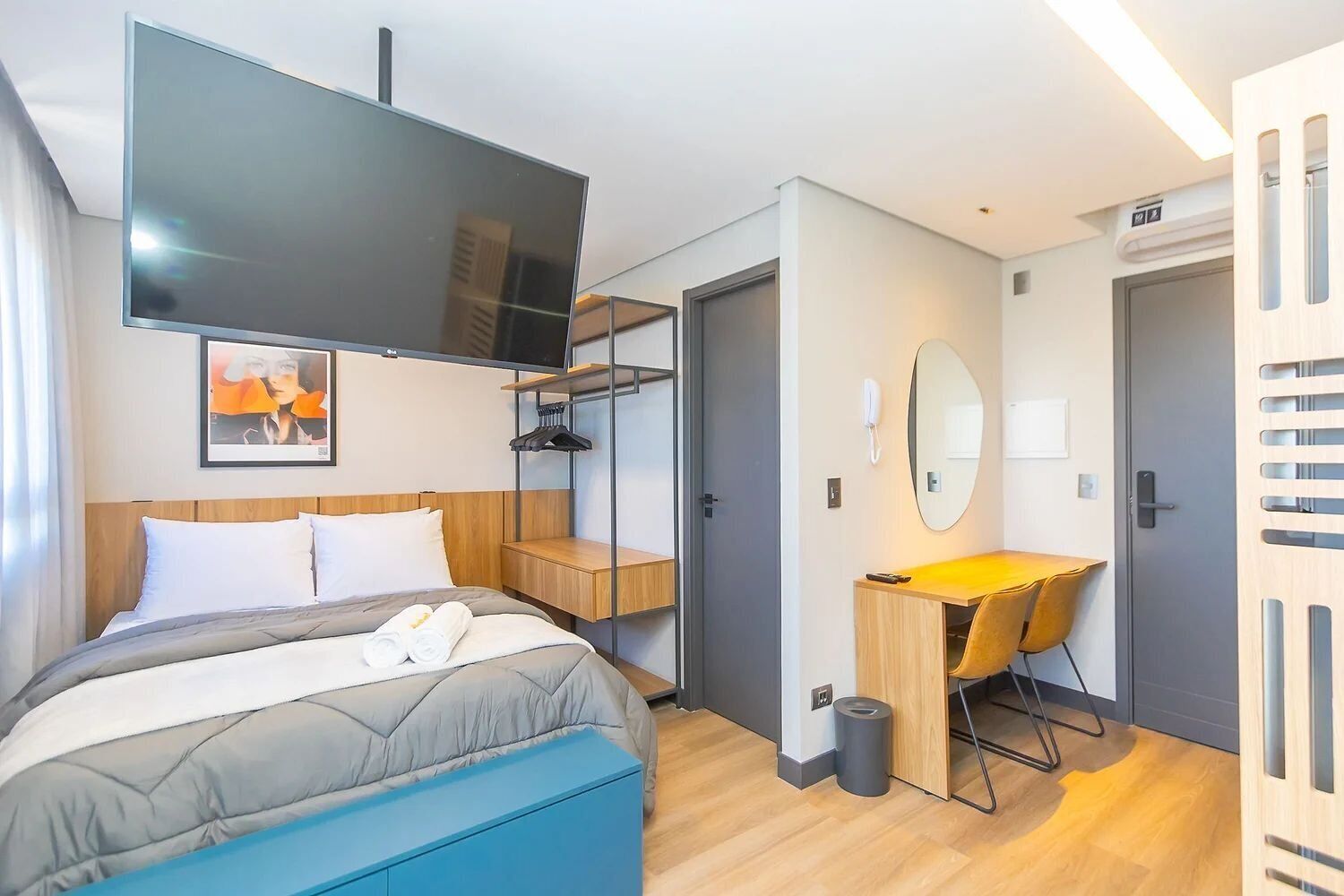 A modern hotel room with a bed, a desk, a chair, a TV, and a bathroom door.