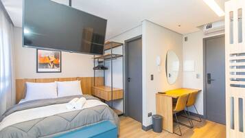 A modern hotel room with a bed, a desk, a chair, a TV, and a bathroom door.