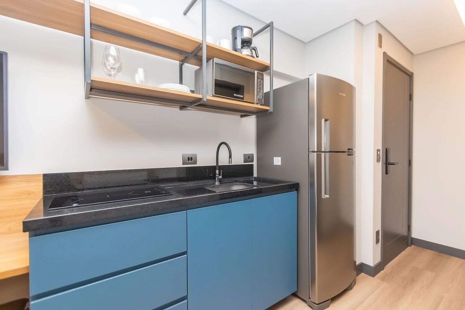 Cocina moderna con refrigerador de acero inoxidable, gabinetes azules, encimera negra y estante para microondas empotrado.