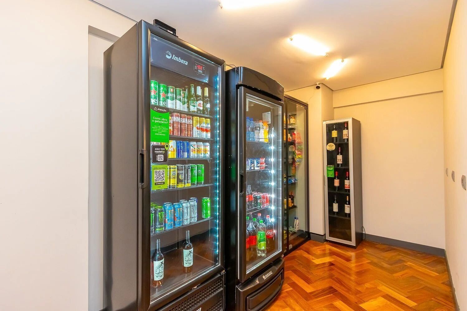 Twee drankautomaten in een gang met houten vloer en een deur op de achtergrond.