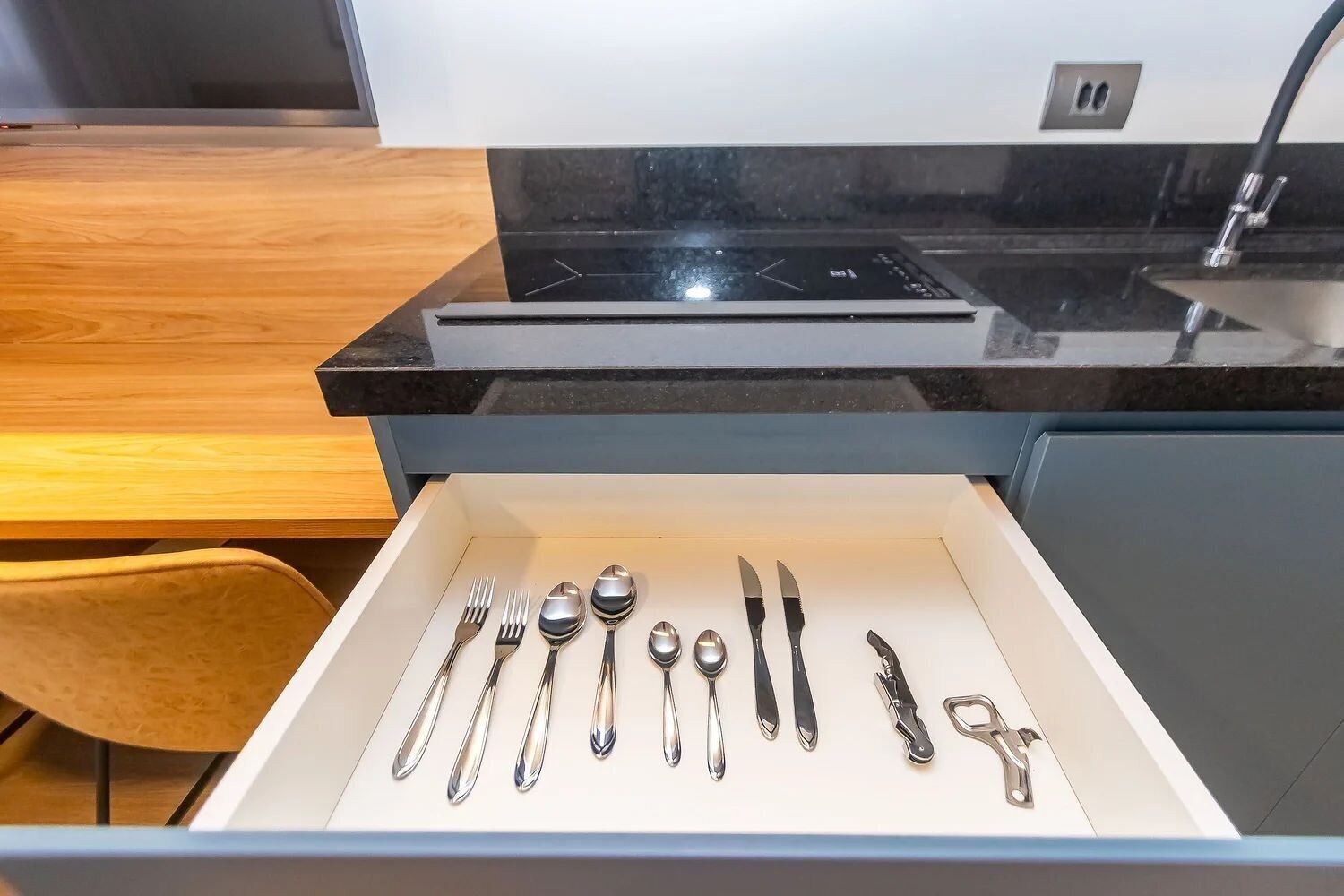 A kitchen drawer with various utensils including forks, spoons, a knife, and a bottle opener.