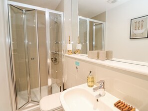 Ein modernes Badezimmer mit einer Duschkabine, einem weißen Waschbecken mit chromfarbenem Wasserhahn und einem Ablagefach für Pflegeprodukte.