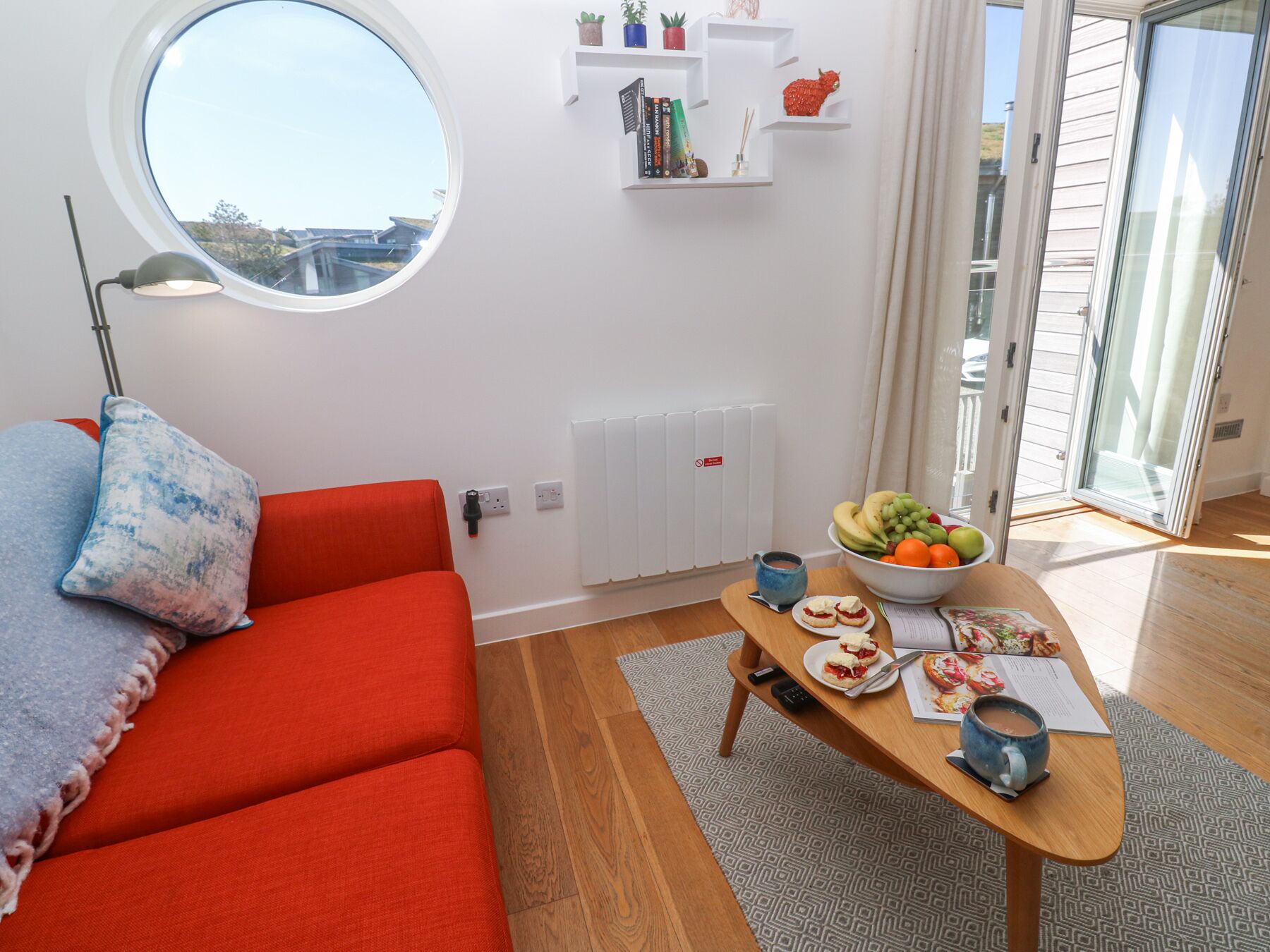 Uma sala de estar moderna com um sofá vermelho, uma janela redonda, uma mesa de jantar com comida e vista para o exterior.