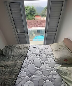 A bedroom with a bed, a window, and a view of a swimming pool outside. - House with pool in Maresias - SP (1) (Sao Sebastiao)
