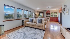 A spacious living area with a beige sofa, a patterned rug, and large windows offering a view of the outdoors. - Charming 1-bedroom house with WiFi, AC , laundry in lovely Snohomish (Snohomish)