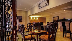 A hotel lobby with a reception desk, a television, and a seating area with wooden chairs and a table. - Brava Hotel (Ibadan)