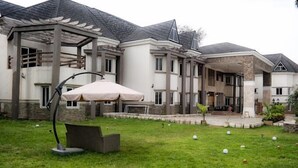 A large, multi-story house with a covered patio area and a lawn with golf balls. - Brava Hotel (Ibadan)