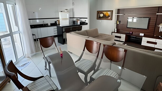 A modern living room with a sofa, TV, and dining area with chairs and a table. - Casa com piscina em Bertioga 1 (Bertioga)