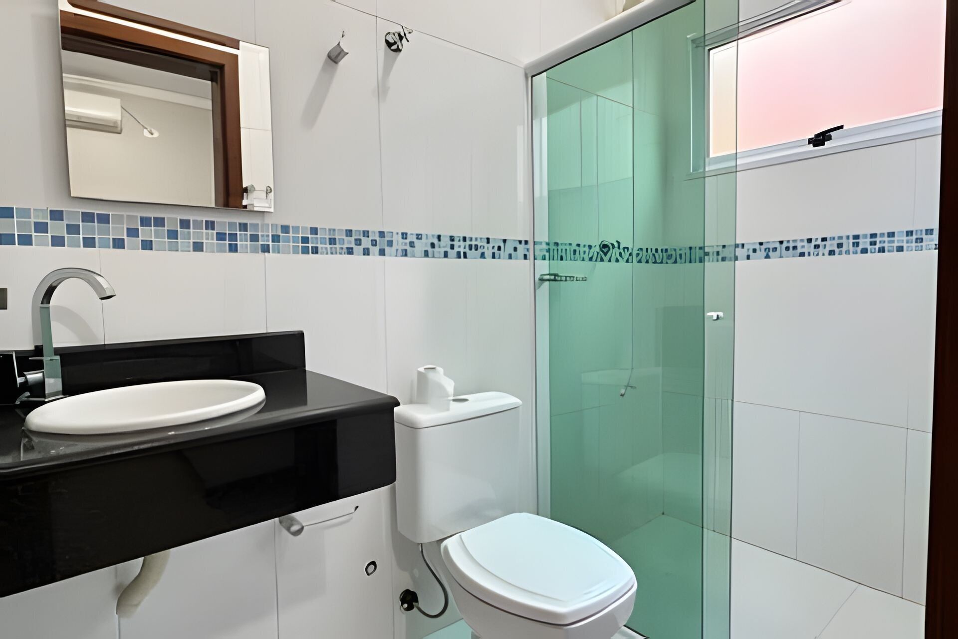 Un baño con lavamanos blanco, encimera negra, inodoro blanco y cabina de ducha con mampara de vidrio.