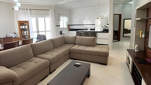 A modern living room with a sectional sofa, a coffee table, and a kitchen in the background. - Casa com piscina em Bertioga 1 (Bertioga)