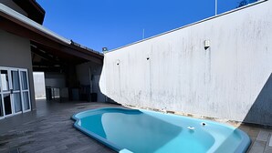 A swimming pool adjacent to a building with a covered parking area. - Casa com piscina em Bertioga 1 (Bertioga)