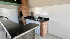 A kitchen with a brick oven, white tiled walls, and a granite countertop. - Casa com piscina em Bertioga 1 (Bertioga)