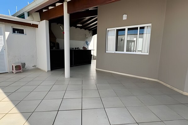 A covered outdoor area with tiled flooring, a reception desk, and a window with curtains. - Casa com piscina em Bertioga 1 (Bertioga)