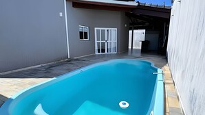 A swimming pool with a tiled deck, a white door, and a window. - Casa com piscina em Bertioga 1 (Bertioga)