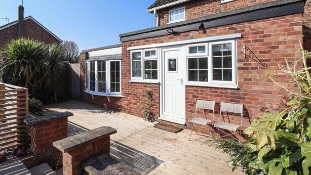 A two-story brick house with a front door, two windows, and a small porch with a bench. - Rose Cottage (Cottingham)