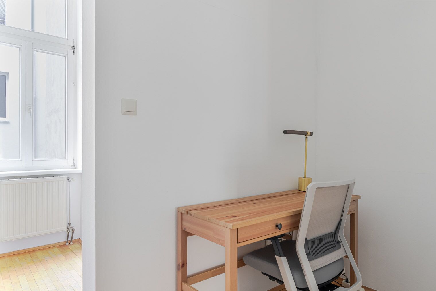 Ein Zimmer mit Holzschreibtisch, Stuhl, Lampe und Fenster.
