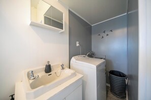 A modern bathroom with a white sink, a mirror, a towel rack, and a black trash bin.