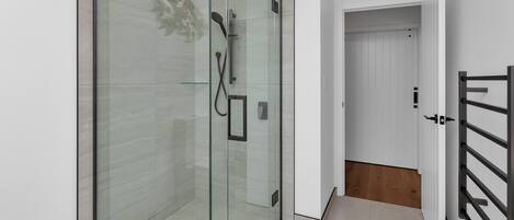A modern bathroom with a glass-enclosed shower, white tiles, and a wooden floor.