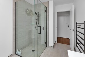 A modern bathroom with a glass-enclosed shower, white tiles, and a wooden floor. - Central Couples Retreat - Mangawhai Heads Unit (Mangawhai)