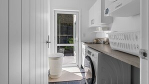 A laundry room with a washing machine, dryer, and a laundry basket. - The Lighthouse - Te Mata Holiday Home (Thames)