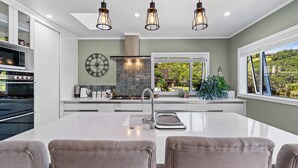A modern kitchen with white cabinetry, a central island, and pendant lighting. - The Lighthouse - Te Mata Holiday Home (Thames)