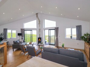 A spacious living room with a high ceiling, large windows, a fireplace, and a view of the outdoors.
