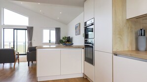 A modern kitchen with white cabinets, a wooden countertop, and a built-in oven. - Jacana (Perranporth)