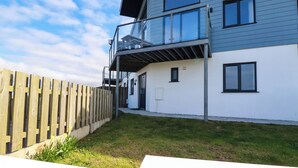 A modern two-story house with a balcony, a wooden fence, and a grassy yard. - Jacana (Perranporth)