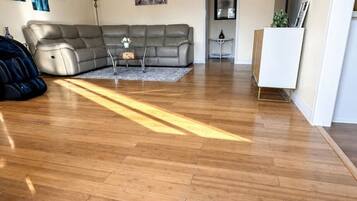 A living room with a grey sectional sofa, a small side table, and a lamp. There is a wooden floor and a door in the background.