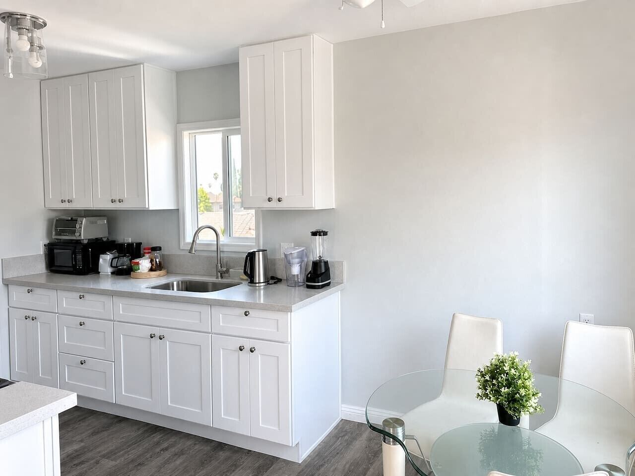 A modern kitchen with white cabinetry, a glass dining table, and a small potted plant.