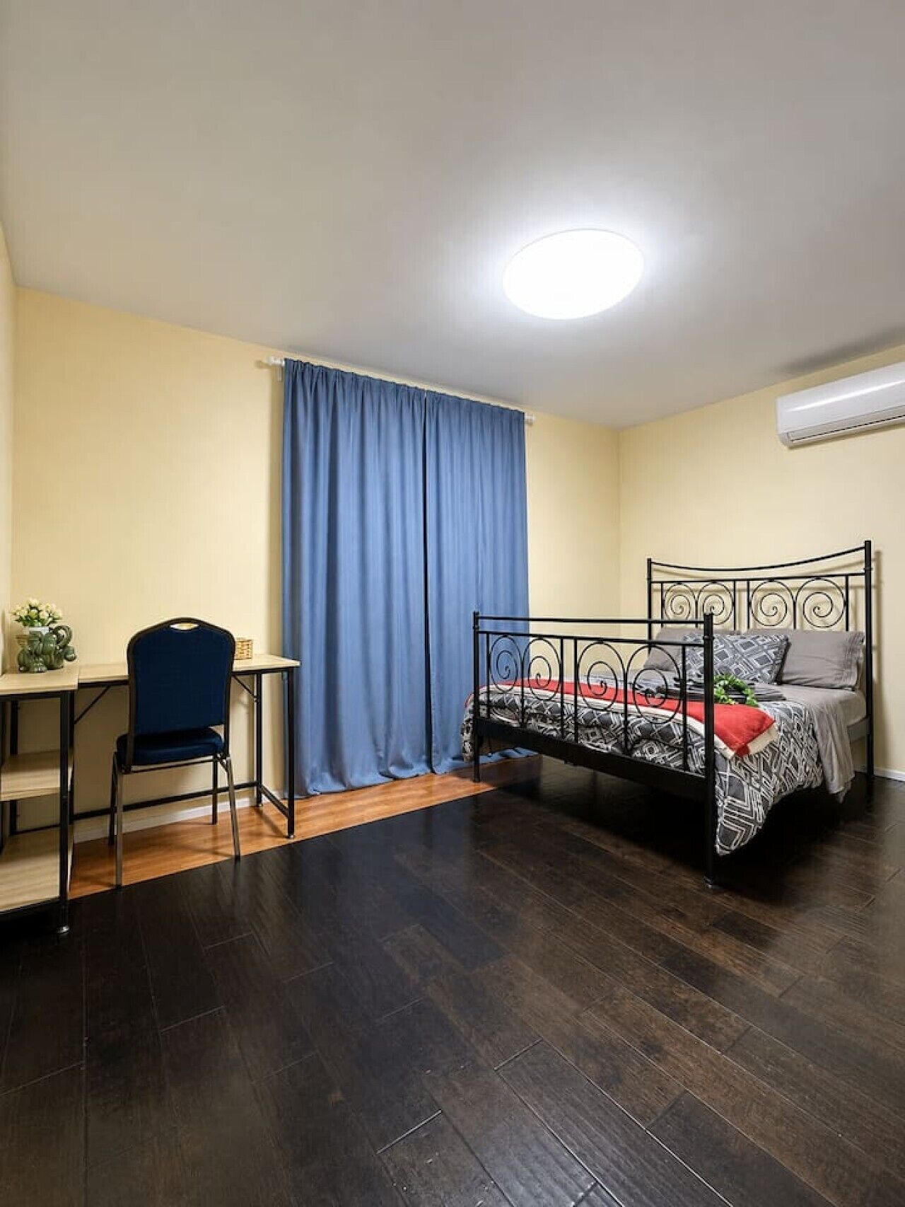 Une pièce comprenant un lit, un bureau, une chaise, un rideau et un appareil de climatisation.