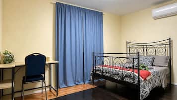 A room with a bed, a desk, a chair, a curtain, and an air conditioning unit.