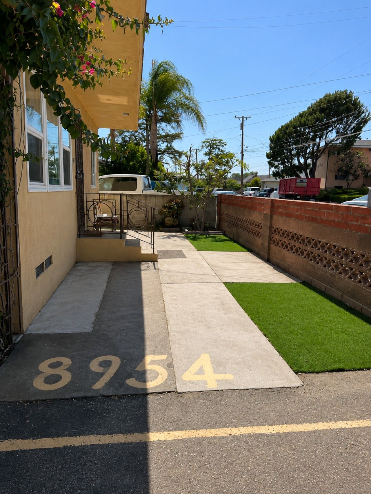 A residential street with a sidewalk, a green lawn, and a building with a beige exterior.