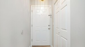 A hallway with a white door, a light fixture above it, and a wooden floor.