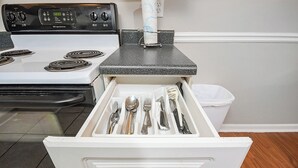 A kitchen with a white stove, a drawer with silverware, and a black countertop.