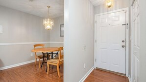 A dining area with a wooden table and chairs, a chandelier, and a white door with a silver handle.