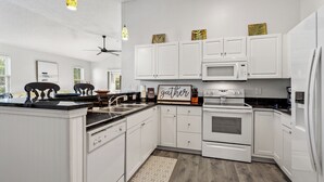 A modern kitchen with white cabinetry, a microwave, an oven, and a ceiling fan. - Ocean Keys 2 Blocks To The Ocean (North Myrtle Beach)