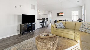 A modern living room with a flat-screen TV, a beige sofa, and a dining area with chairs and a table. - Ocean Keys 2 Blocks To The Ocean (North Myrtle Beach)