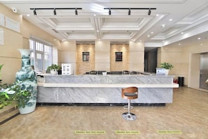 A hotel reception area with a marble counter, a large vase, and potted plants. - Yong Xu Hotel (Antu)