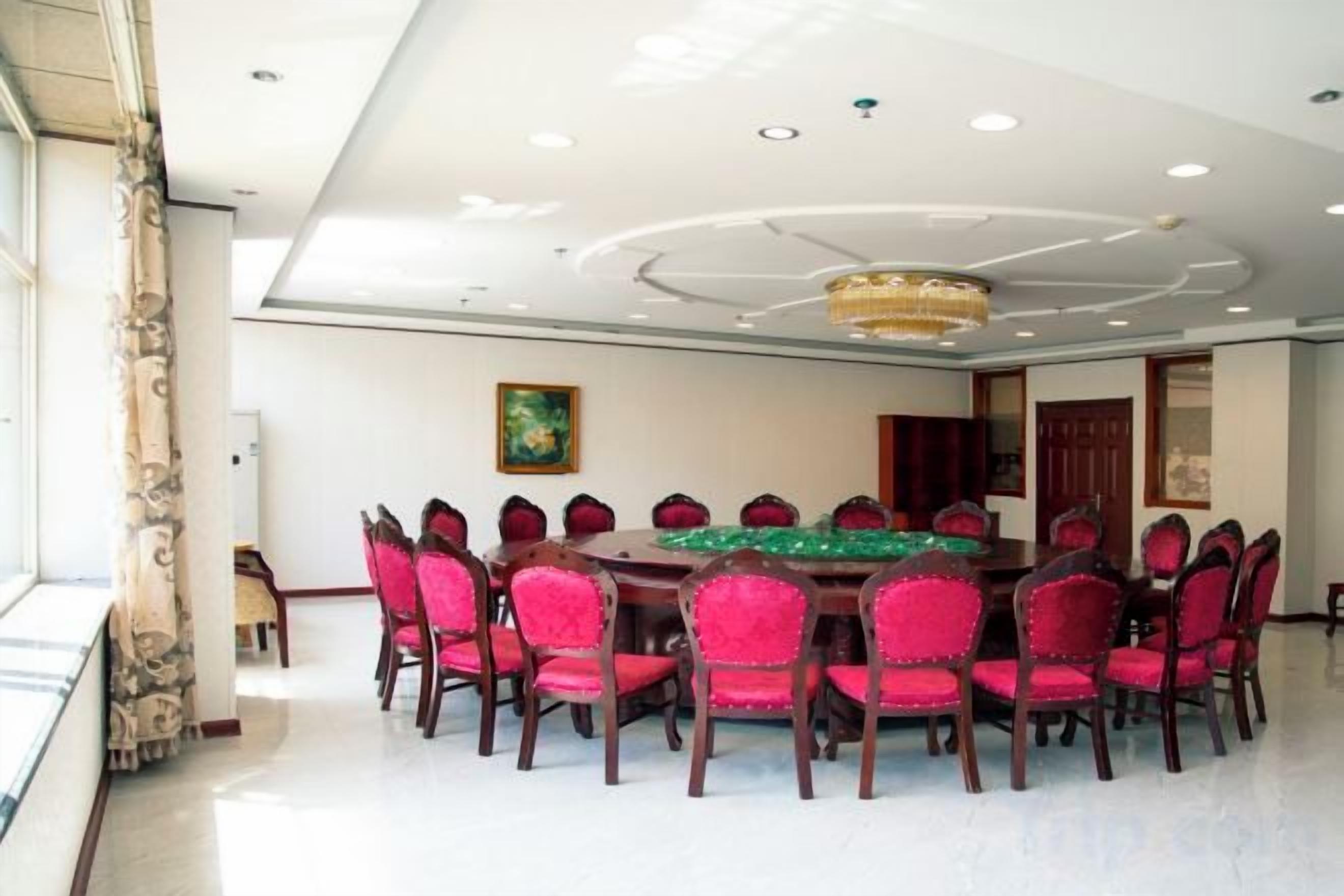A conference room with a round table, red chairs, and a chandelier.