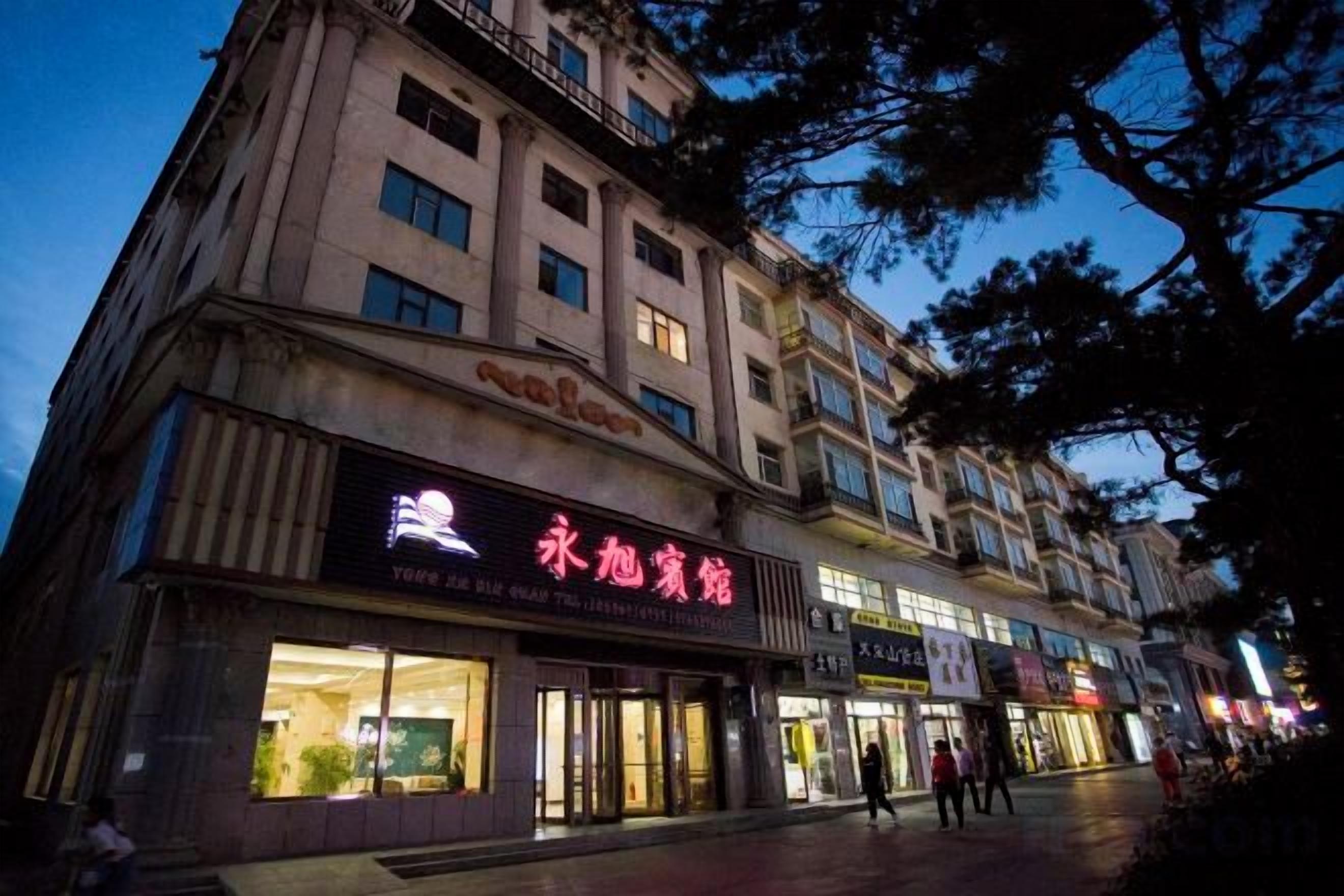 Un edificio de varios pisos con señalización iluminada, escaparate y una acera para peatones.