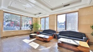 Una hall moderna con ampie finestre, un divano in pelle nera e un tavolino in legno.