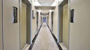 Corridoio di un hotel con porte contrassegnate dai numeri delle stanze, un pavimento a motivi e un lampadario.