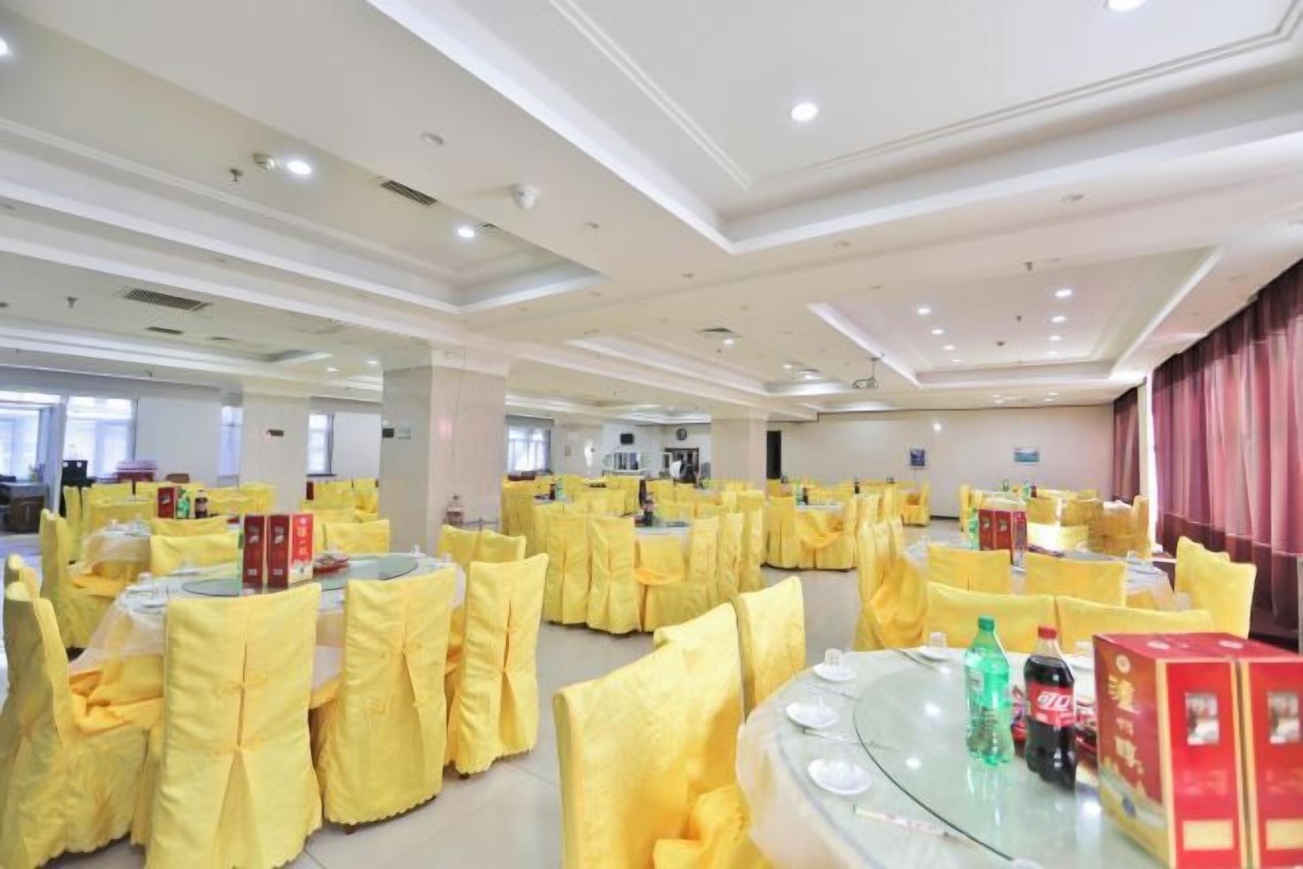 A banquet hall with round tables covered in yellow tablecloths, arranged in rows.